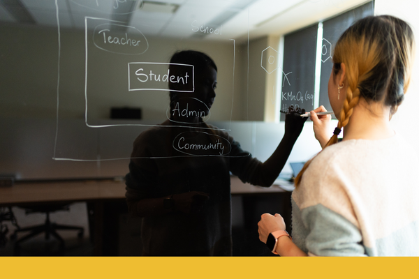 Undergraduate student pictured from behind is writing on a blackboard