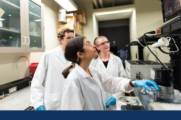 Three students look at a computer monitor as they perform a Chemistry experiment