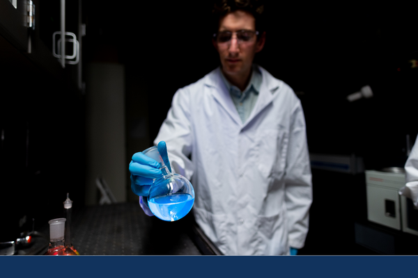 A student holds a flask of blue chemicals towards the camera