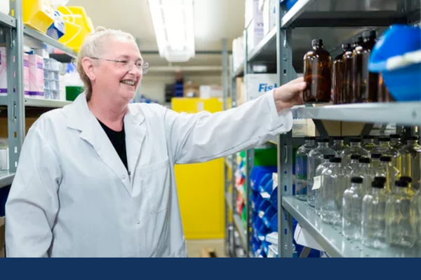 Operations assistant retrieves a brown bottle from a shelf containing various empty bottles for use in chemical experiments