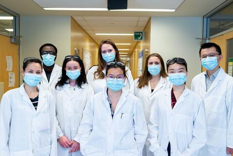 Group of students wearing face masks and lab coats pose for the camera