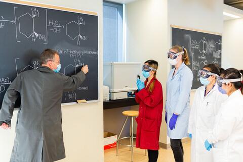 Faculty member writes on chalkboard with students watching