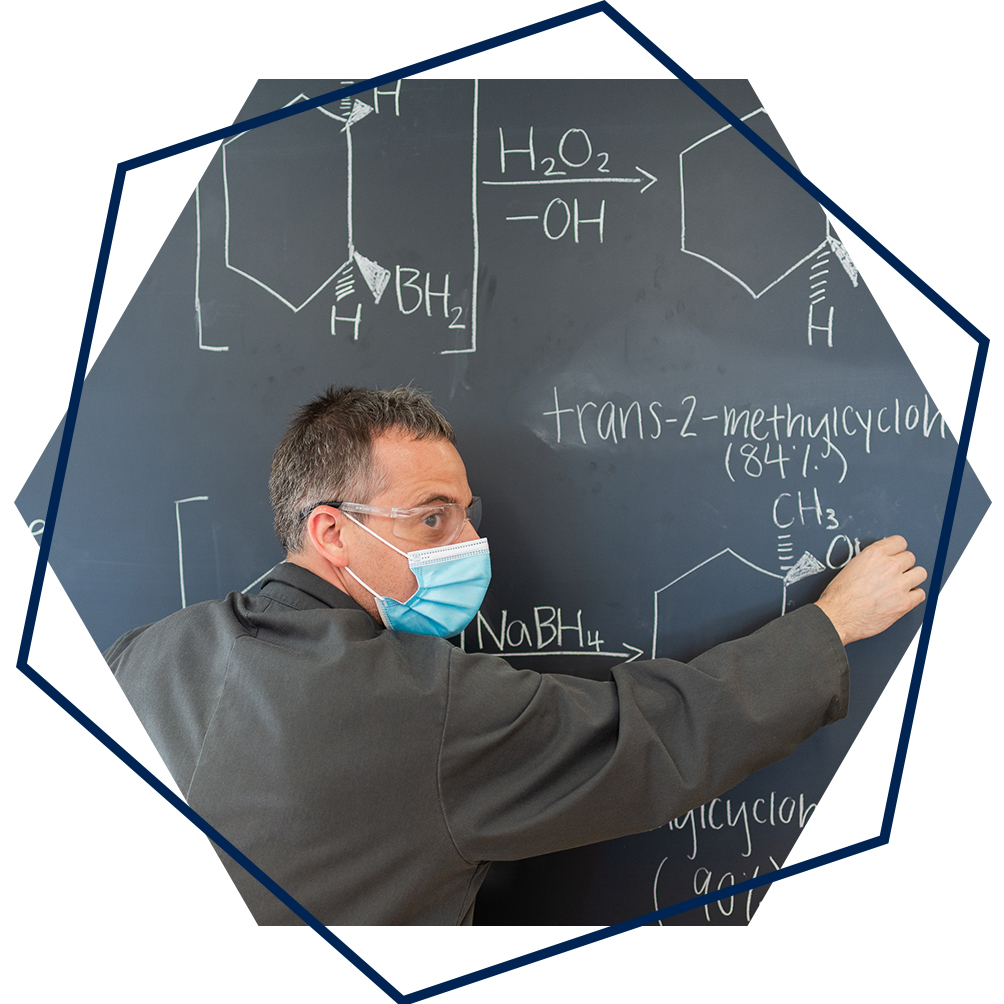 Man wearing face mask is writing chemical equations on a blackboard