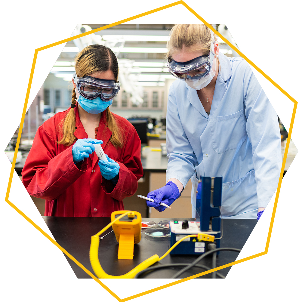 Two undergraduate students work together at a bench with flasks and vials as part of a chemistry experiment
