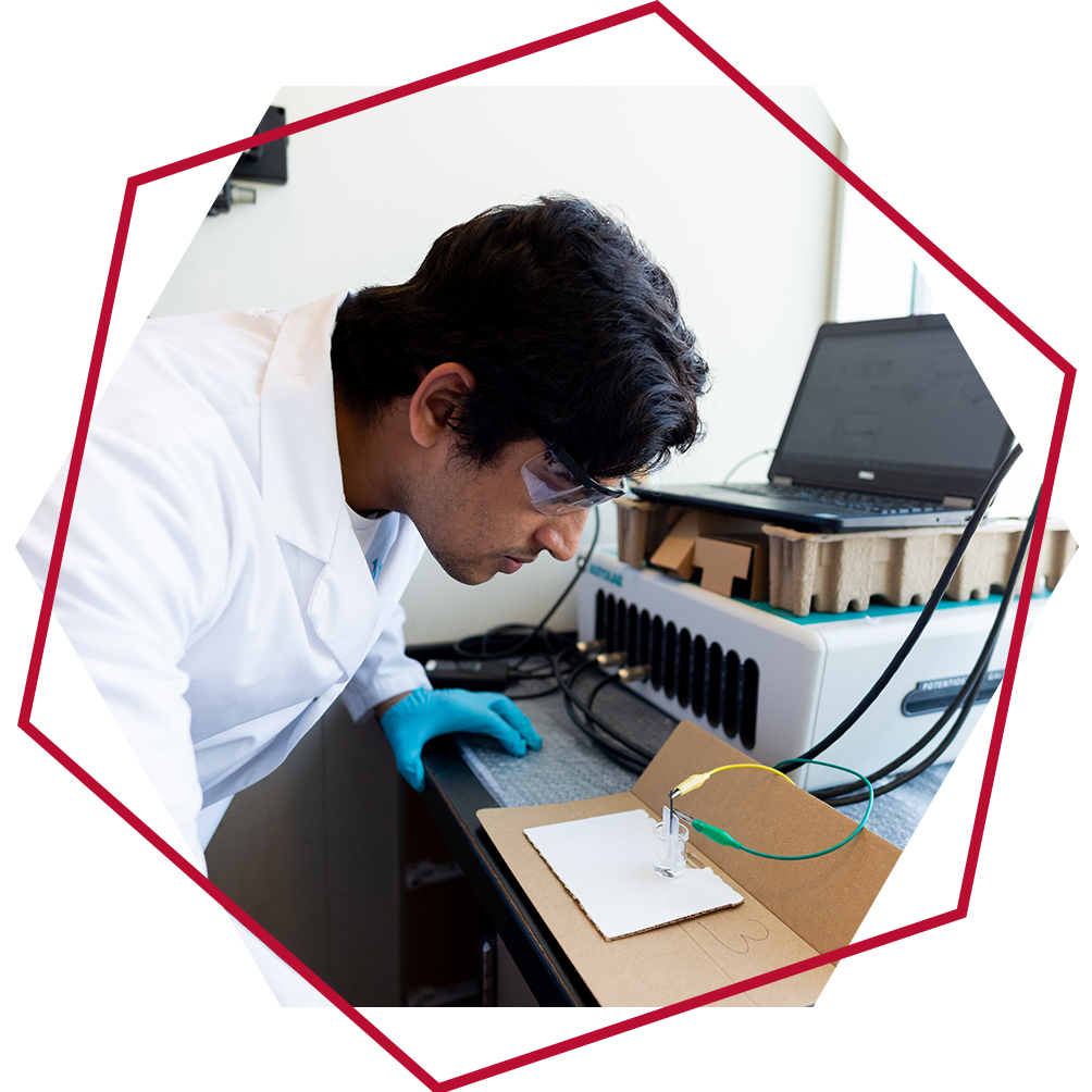 Graduate student wearing safety goggles performs chemistry equipment using wires