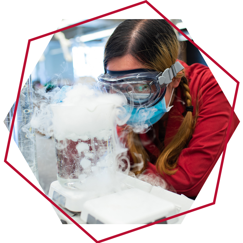 Graduate student wearing safety goggles watches a flask which is steaming