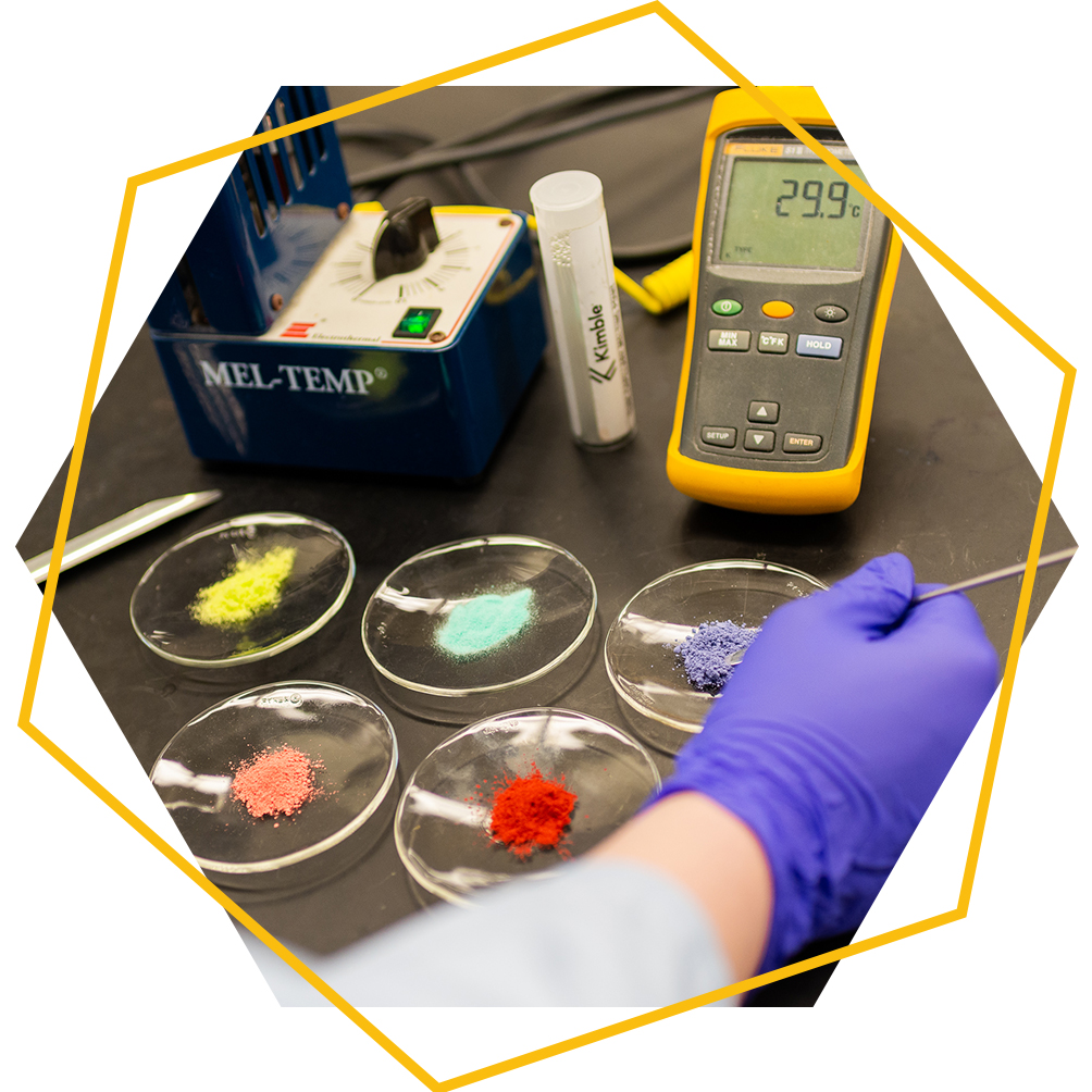 Gloved hands measuring and weighing colored powders