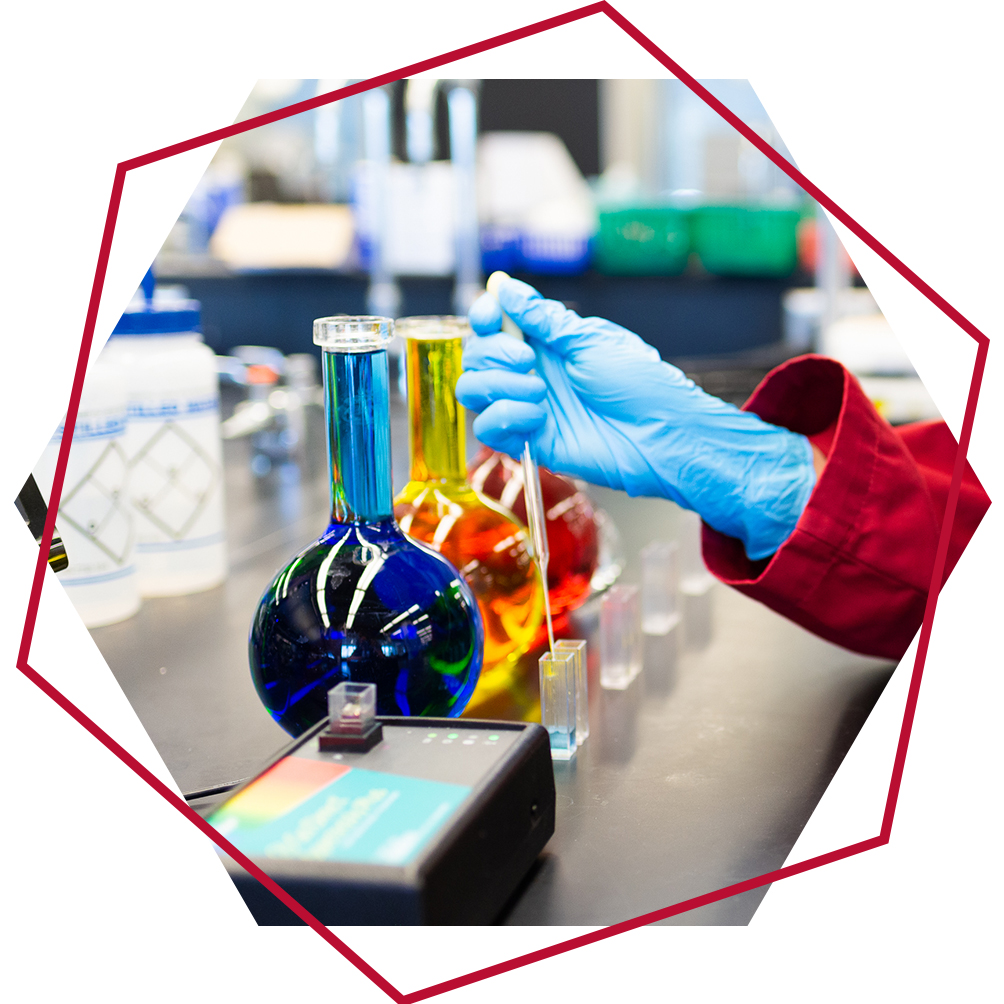 Gloved hands measuring different coloured liquid chemicals into flasks